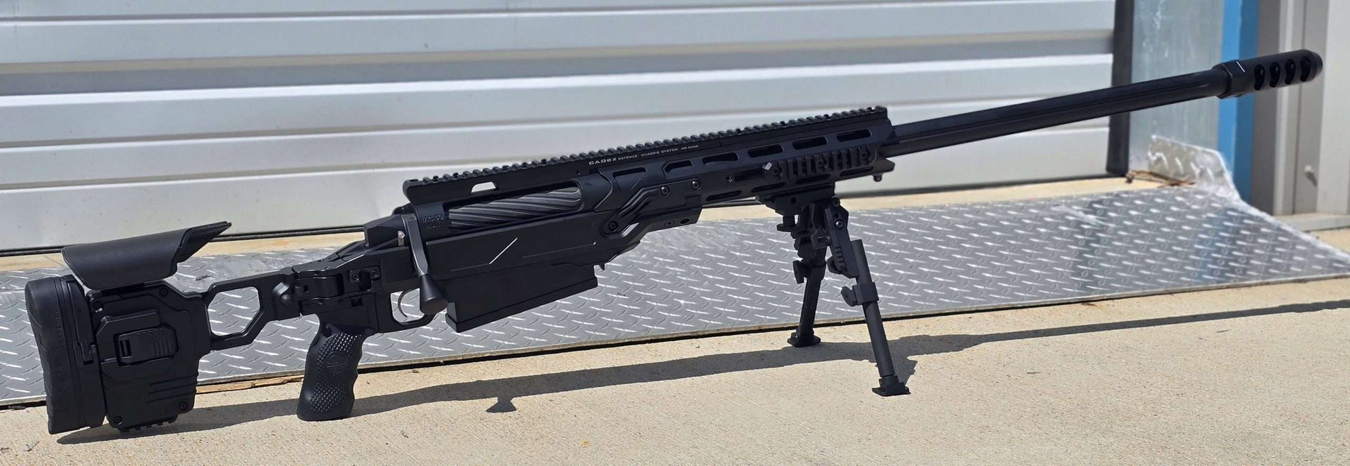 A modern bolt-action sniper rifle with an olive drab chassis, the B&B Firearms MCMILLAN TAC50C features a tactical adjustable stock, a black pistol grip, a twisted fluted barrel, and an expansion muzzle brake. This .50 BMG tactical rifle also includes a bipod for stability and a Picatinny rail for mounting optics.