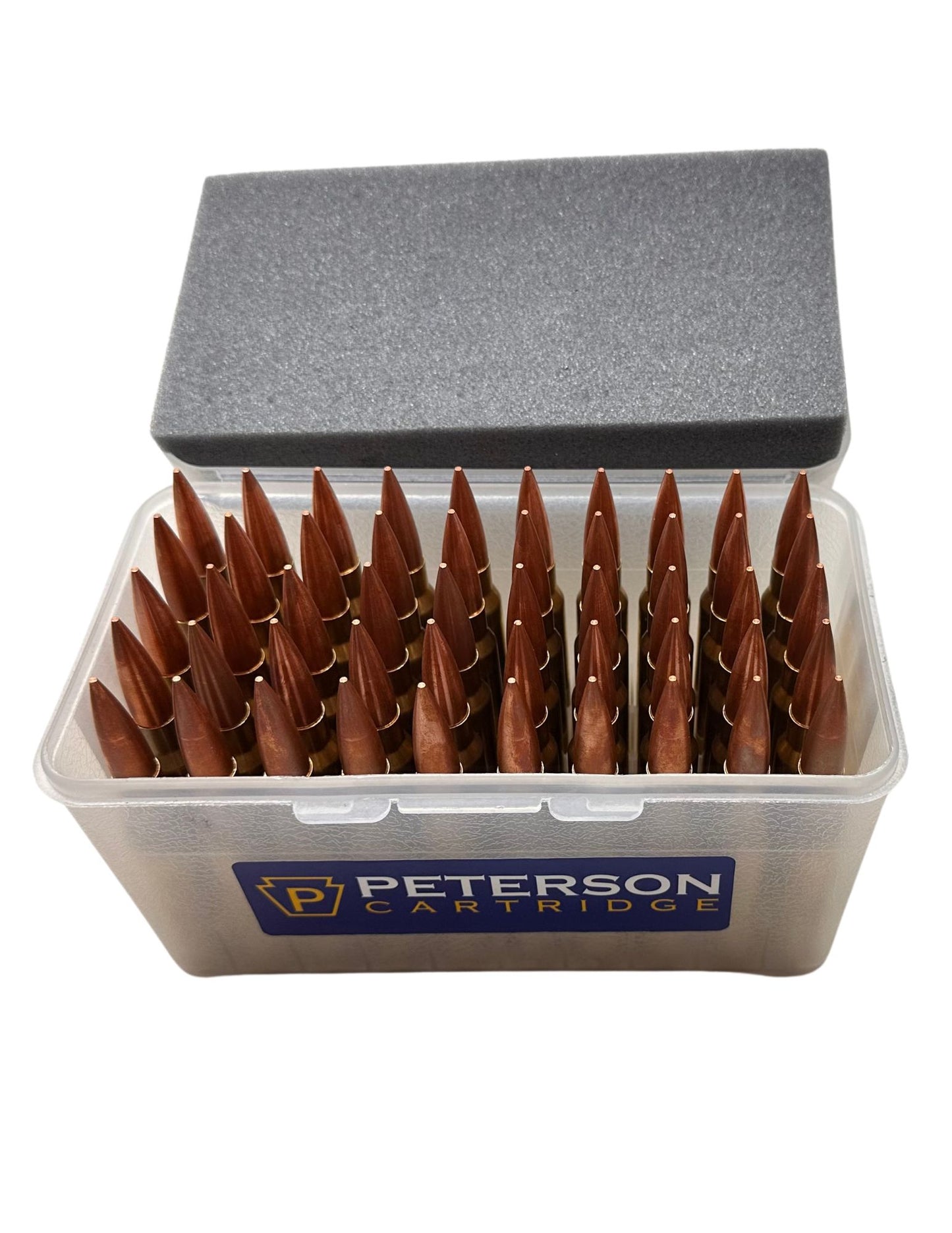 A transparent plastic ammunition box from B&B Firearms containing multiple rounds of .408/419 gr Match rifle ammunition with brass casings and copper nickel alloy bullets. Two additional rounds stand upright next to the box. A blue label on the box reads "Peterson Cartridge".