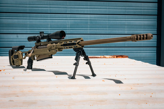 A modern bolt-action sniper rifle with an olive drab chassis, the B&B Firearms MCMILLAN TAC50C features a tactical adjustable stock, a black pistol grip, a twisted fluted barrel, and an expansion muzzle brake. This .50 BMG tactical rifle also includes a bipod for stability and a Picatinny rail for mounting optics.