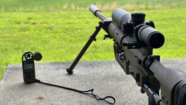 Riflescope with attached device on a concrete surface with a grassy field in the background