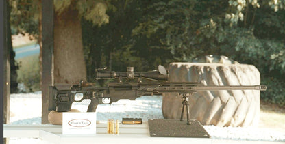 The lightweight **Cheytac M300 Praetorian sniper rifle by B&B Firearms**, favored by competitive shooters, features a long barrel with a bipod near the muzzle, a large scope on top, and a camouflage-patterned stock. Its ergonomic design includes an adjustable cheek rest and a magazine protruding from the bottom. The background is white.