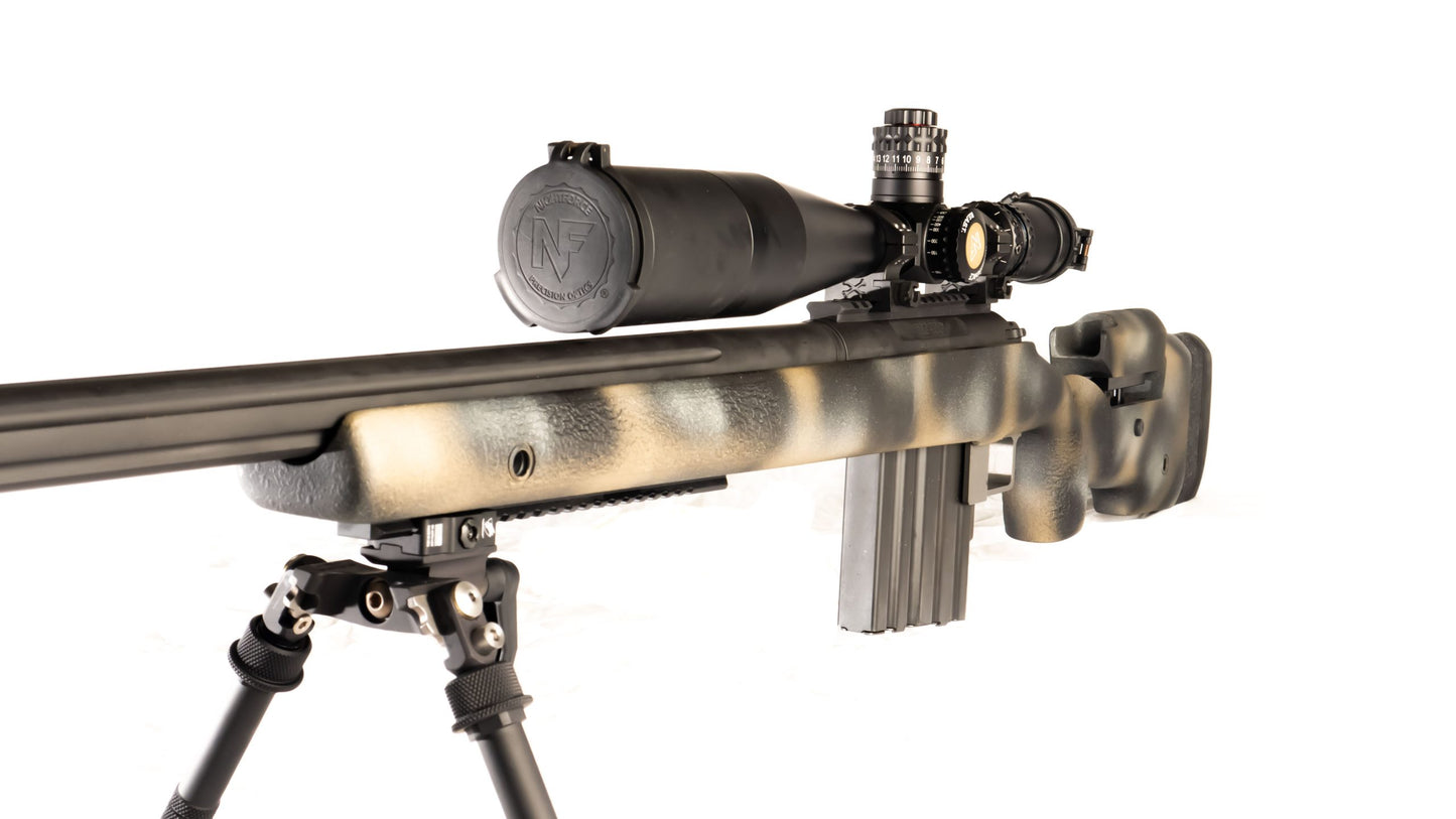 The lightweight **Cheytac M300 Praetorian sniper rifle by B&B Firearms**, favored by competitive shooters, features a long barrel with a bipod near the muzzle, a large scope on top, and a camouflage-patterned stock. Its ergonomic design includes an adjustable cheek rest and a magazine protruding from the bottom. The background is white.